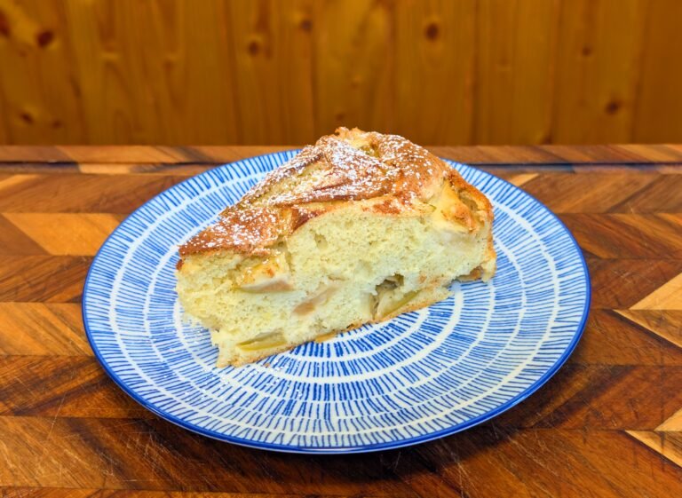 A slice of Russian Apple Sharlotka [Яблочная шарлотка] topped with powdered sugar on a blue patterned plate.