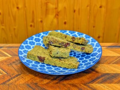 Sliced matcha chocolate bars with melted dark chocolate chunks stacked on a blue and white patterned plate against a wooden background.