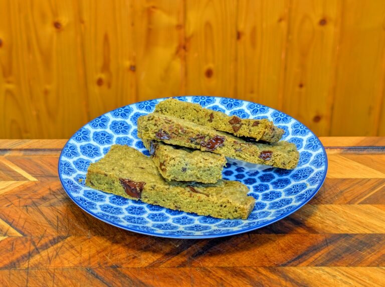 Sliced matcha chocolate bars with melted dark chocolate chunks stacked on a blue and white patterned plate against a wooden background.
