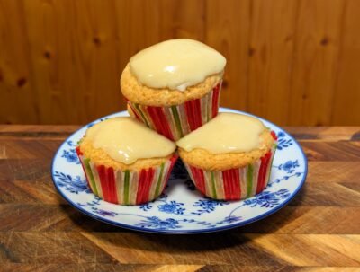 Close-up of three glazed lemon cupcakes stacked in a pyramid on a blue and white floral plate.