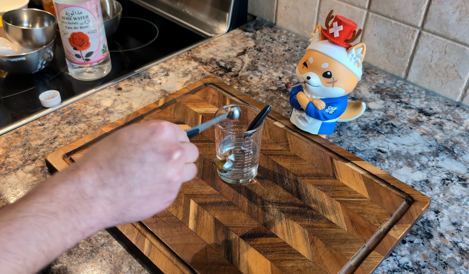 Measuring rose water with a small spoon into a glass measuring beaker for lemon cupcake batter.