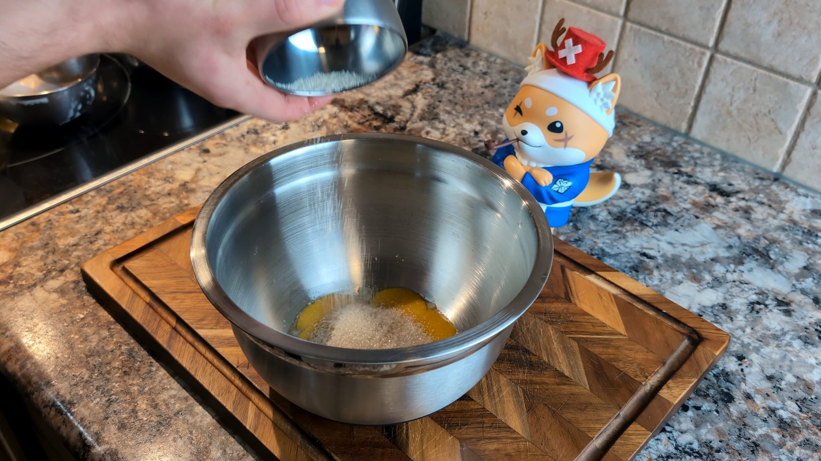 Pouring white granulated sugar from a small metal cup into a bowl of fresh egg yolks.
