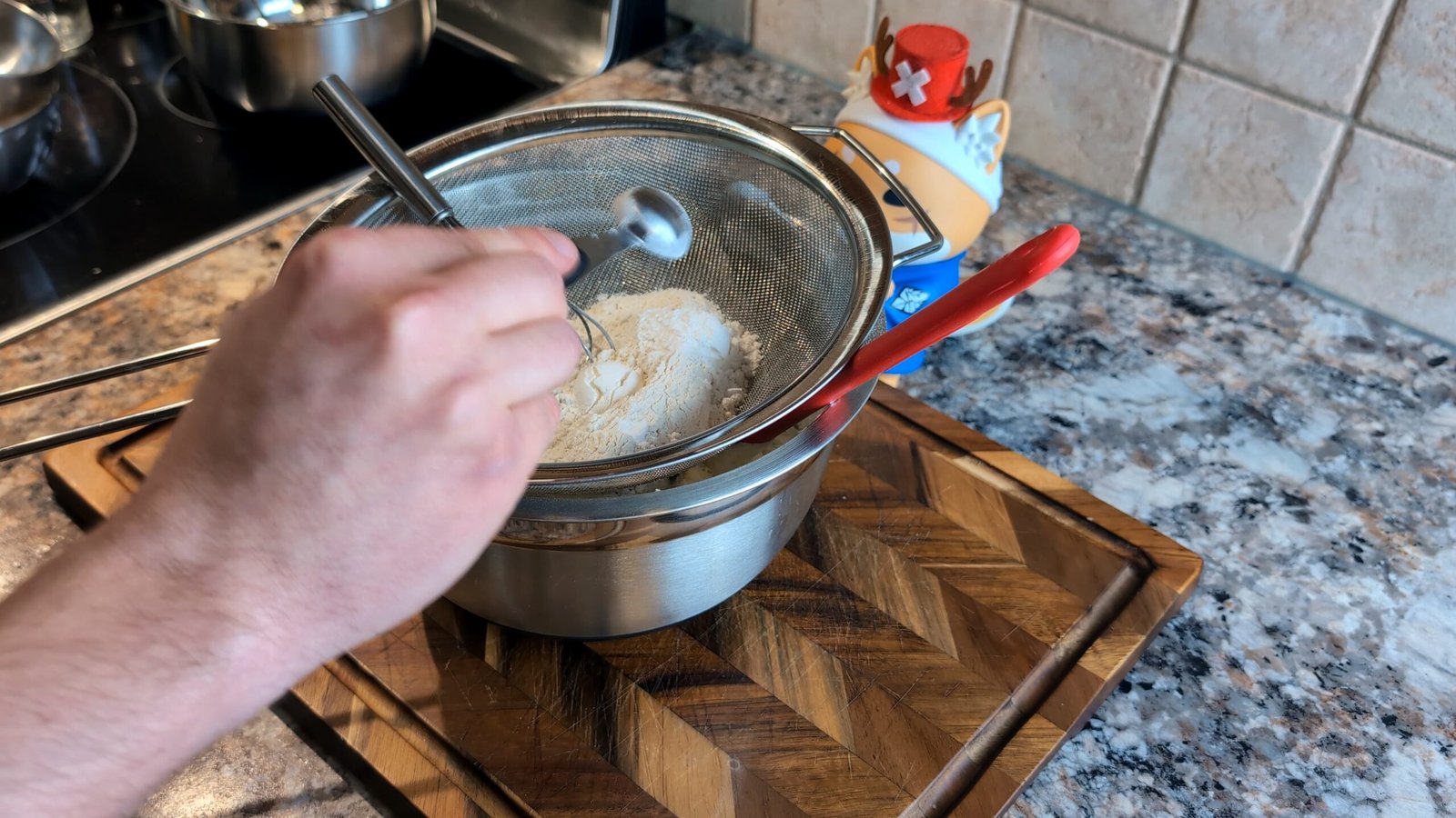 Adding a small measuring spoonful of baking powder into a mesh sieve over a bowl of dry ingredients.