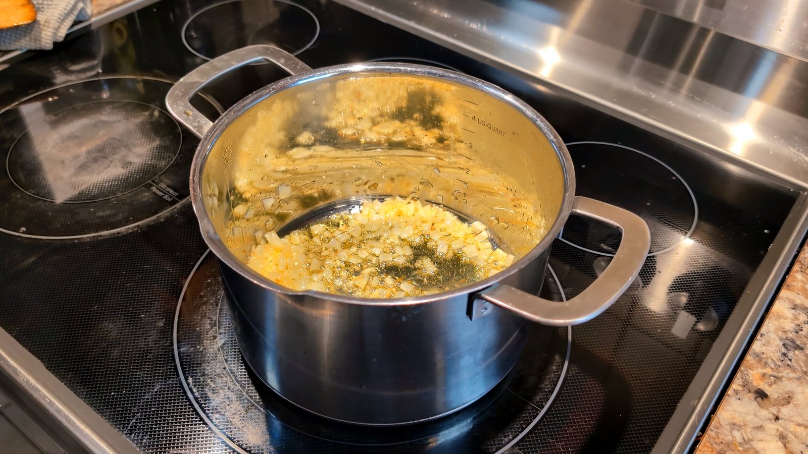 Sautéing diced onions in a stainless steel pot on a glass-top stove to build the base of the masala sauce.