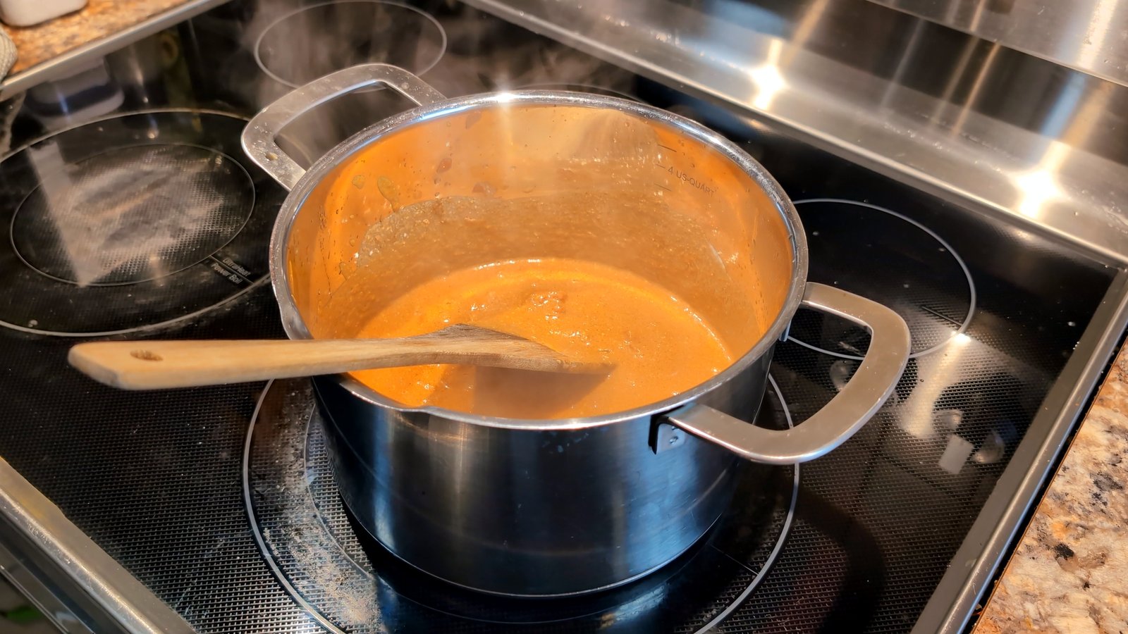 A smooth, rich gobi makhani sauce simmering gently in a pot with a wooden spoon resting inside.
