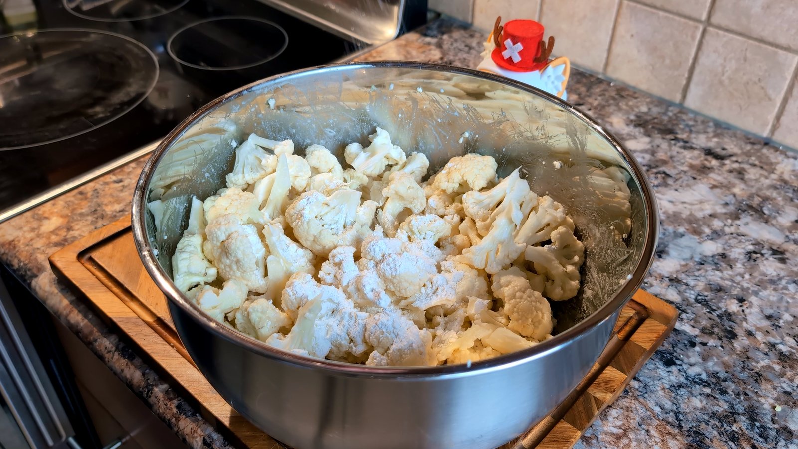 Raw cauliflower florets sprinkled with a dry flour mixture in a large stainless steel bowl.