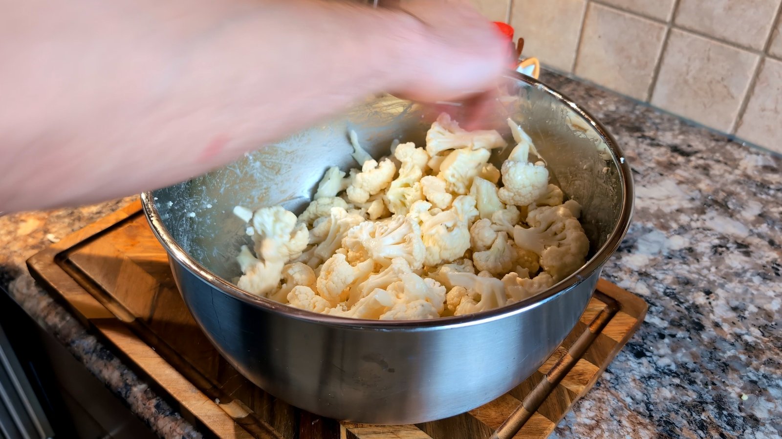 Tossing cauliflower florets by hand in a stainless steel bowl to ensure they are evenly coated.