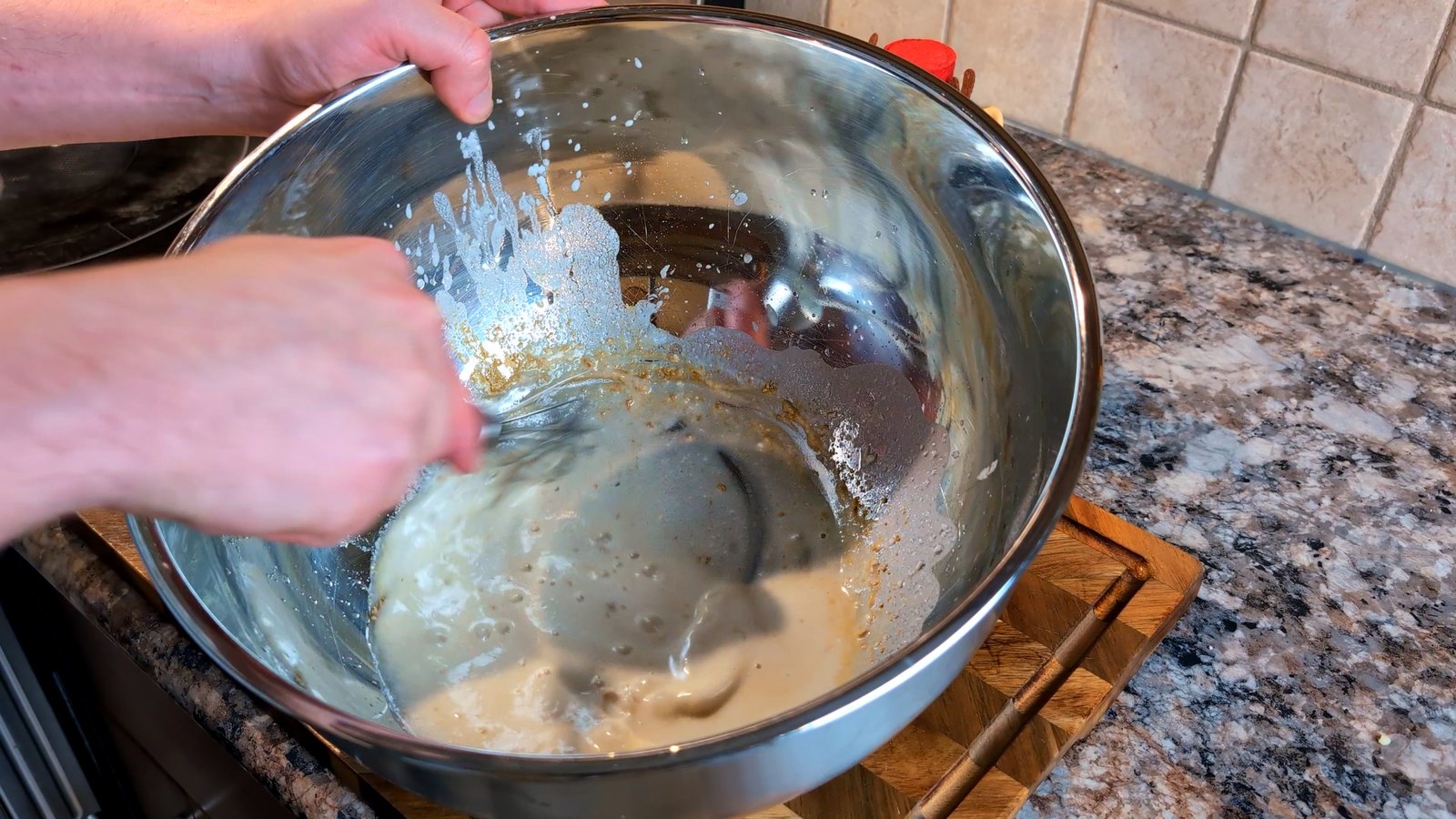 Whisking a light batter in a large stainless steel mixing bowl to coat the cauliflower.